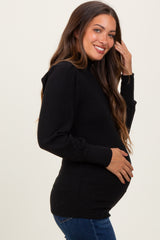 woman wearing a black ribbed maternity sweater and holding her baby bump while smiling