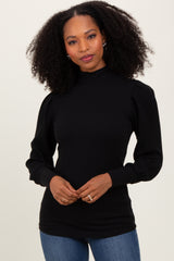 woman wearing a black ribbed turtleneck sweater with puff sleeves and paired with blue jeans