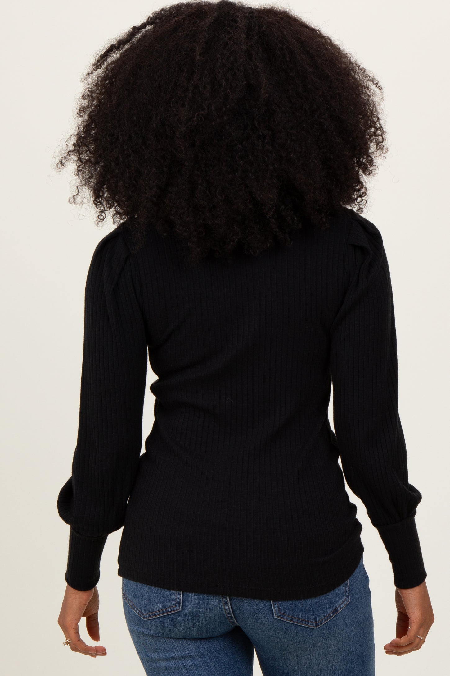 woman wearing a black ribbed long sleeve top with puffed shoulders and back view, paired with blue jeans