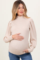 woman wearing a beige ribbed maternity sweater with puffed sleeves and holding her baby bump