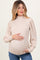 woman wearing a beige ribbed maternity sweater with puffed sleeves and holding her baby bump