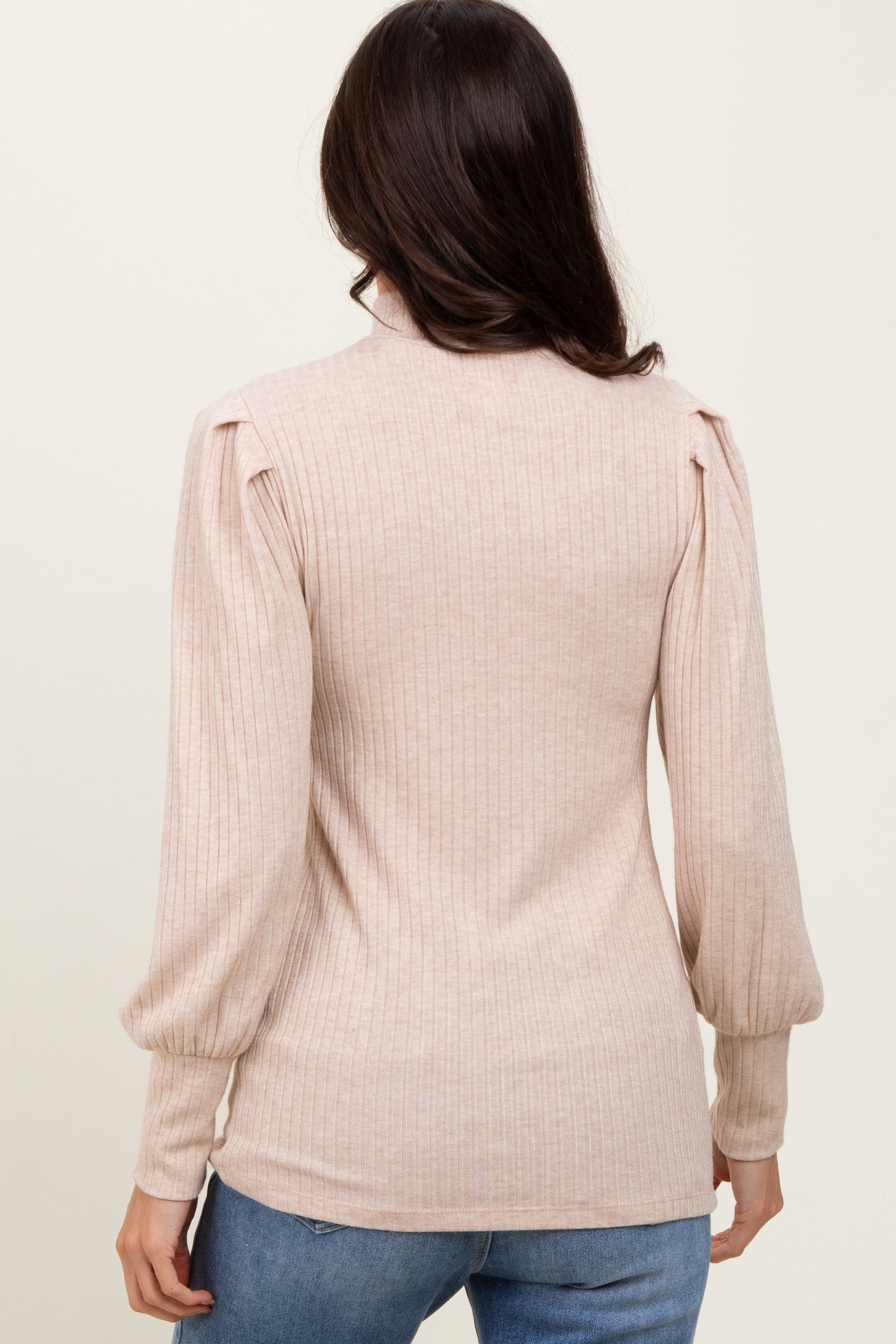 woman wearing a light beige ribbed sweater with puffed sleeves and a fitted silhouette, seen from the back
