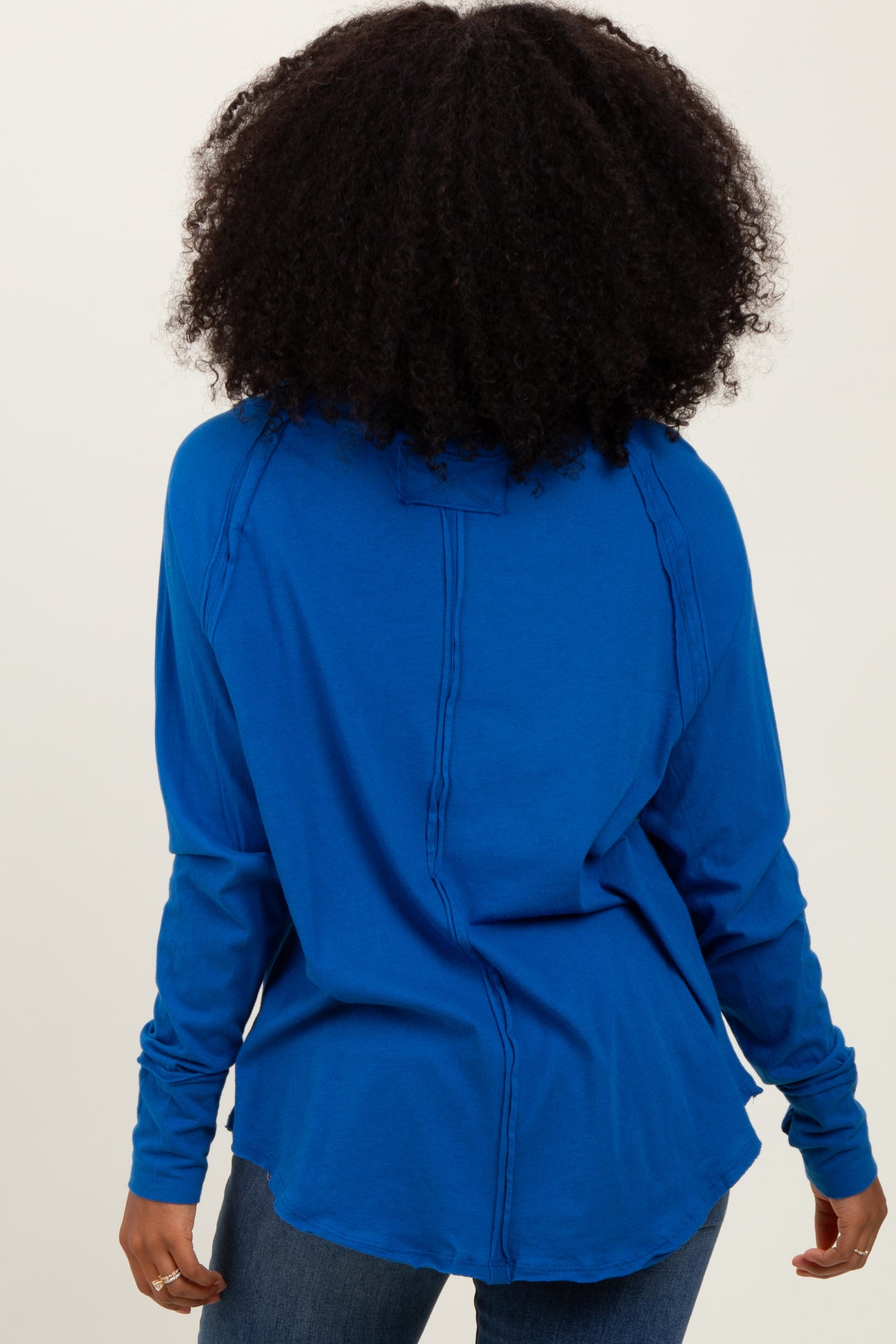 woman wearing a blue long sleeve top with a relaxed fit and seam detailing, viewed from the back