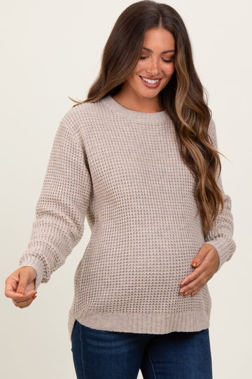 woman wearing a beige knit maternity sweater with a rounded neckline and long sleeves, showing a baby bump