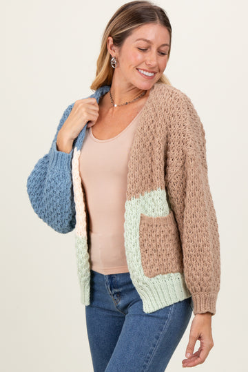 woman wearing a chunky knit cardigan in tan, blue, and mint with a pocket, paired with a nude tank top and jeans