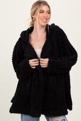 woman wearing a black plush hooded cardigan, smiling and holding it open over a beige top