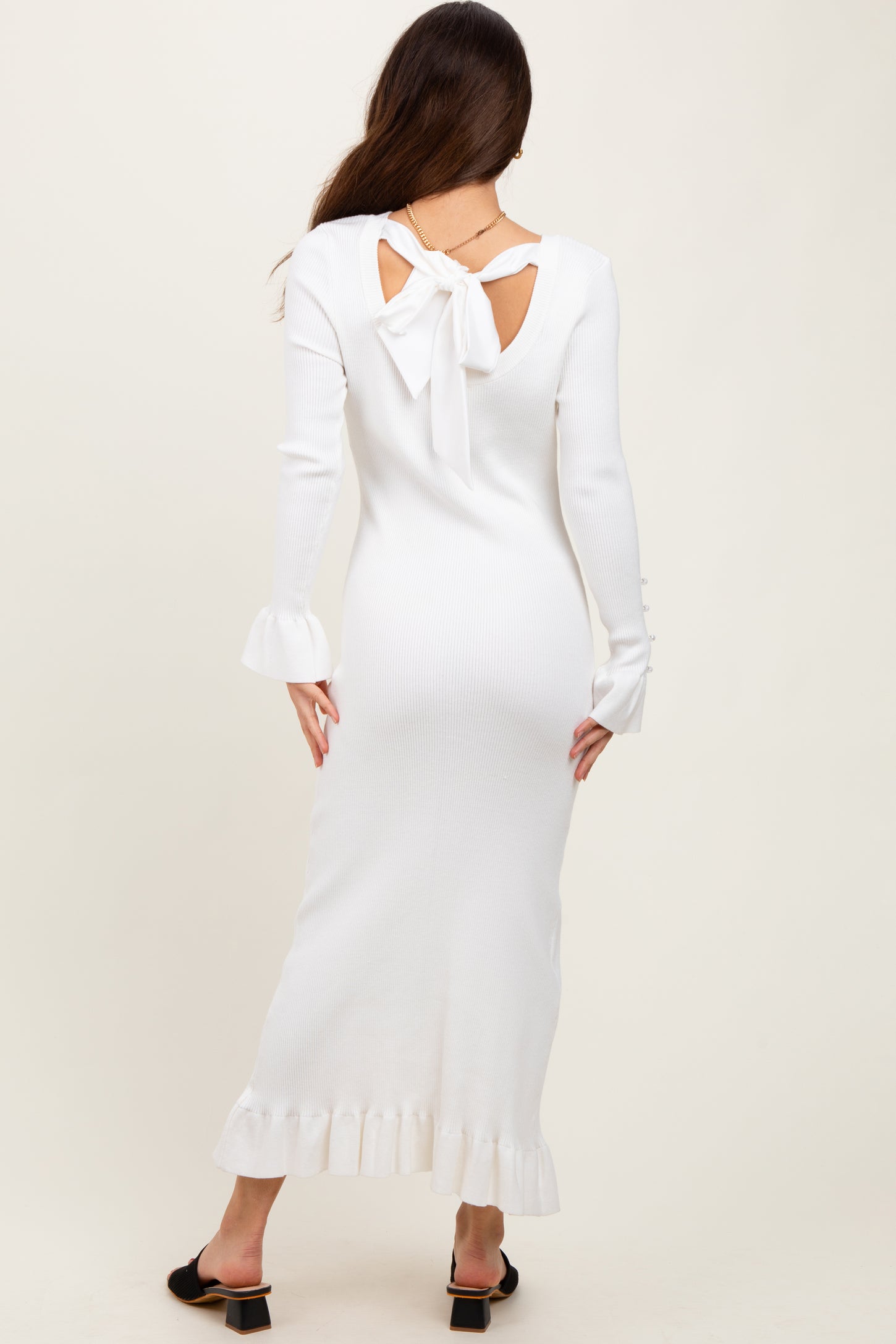 woman wearing a white ribbed long sleeve dress with a bow detail at the back and ruffle hemline