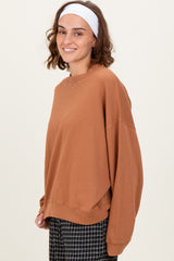 woman wearing a cozy rust-colored oversized sweatshirt with long sleeves and side slits, styled with a white headband