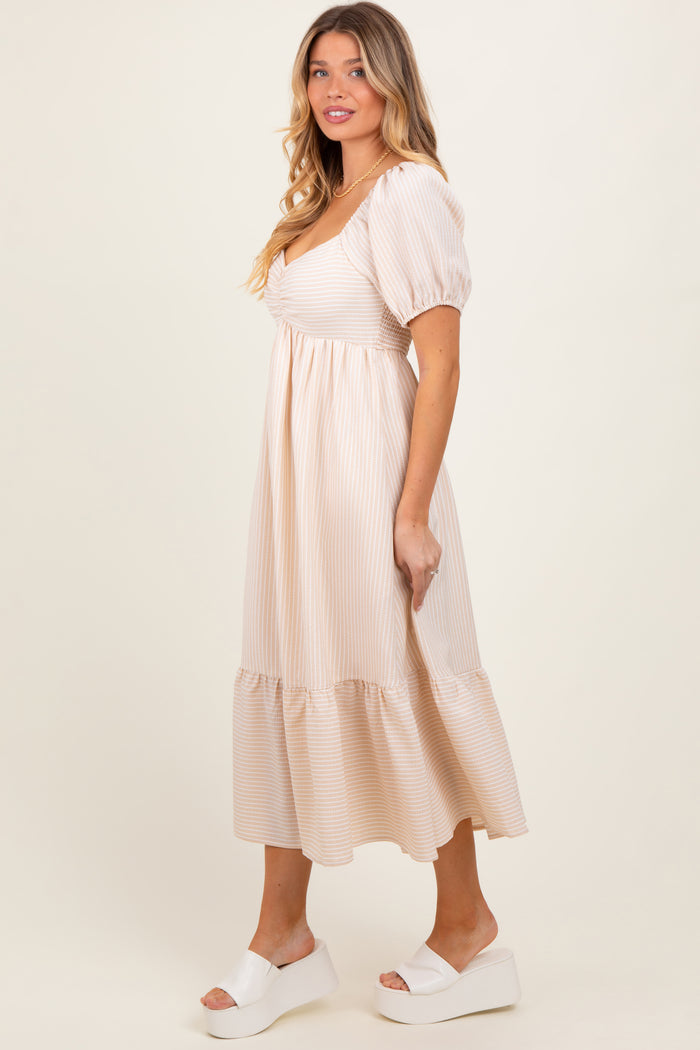woman wearing a cream striped midi dress with puff sleeves and a tiered hem, standing sideways on a light background
