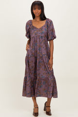 woman wearing a purple floral midi dress with puff sleeves and a tiered skirt, standing and smiling