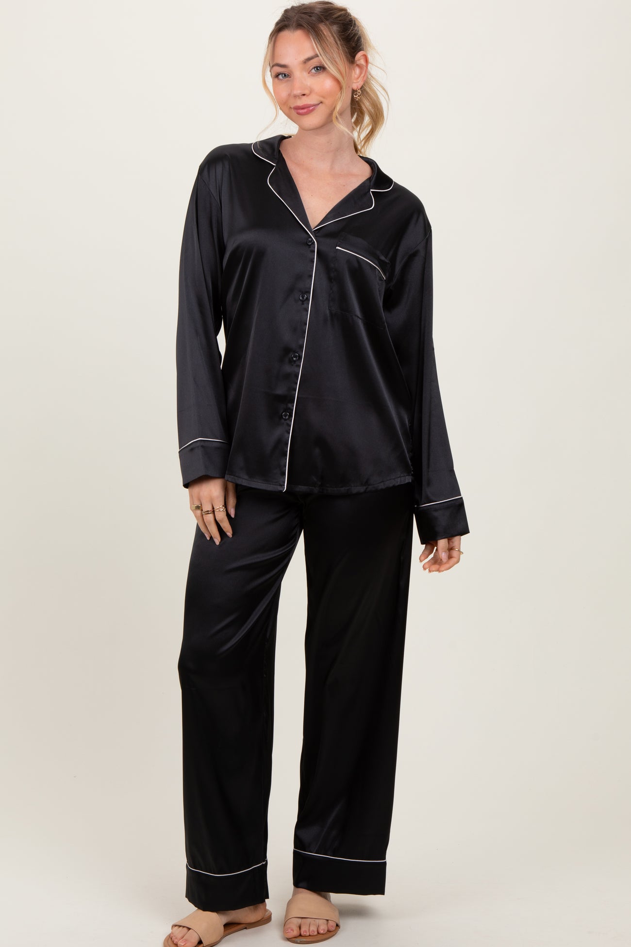 woman wearing a black satin pajama set with white piping, featuring long sleeves and wide-leg pants