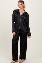 woman wearing a black satin pajama set with white piping, featuring long sleeves and wide-leg pants