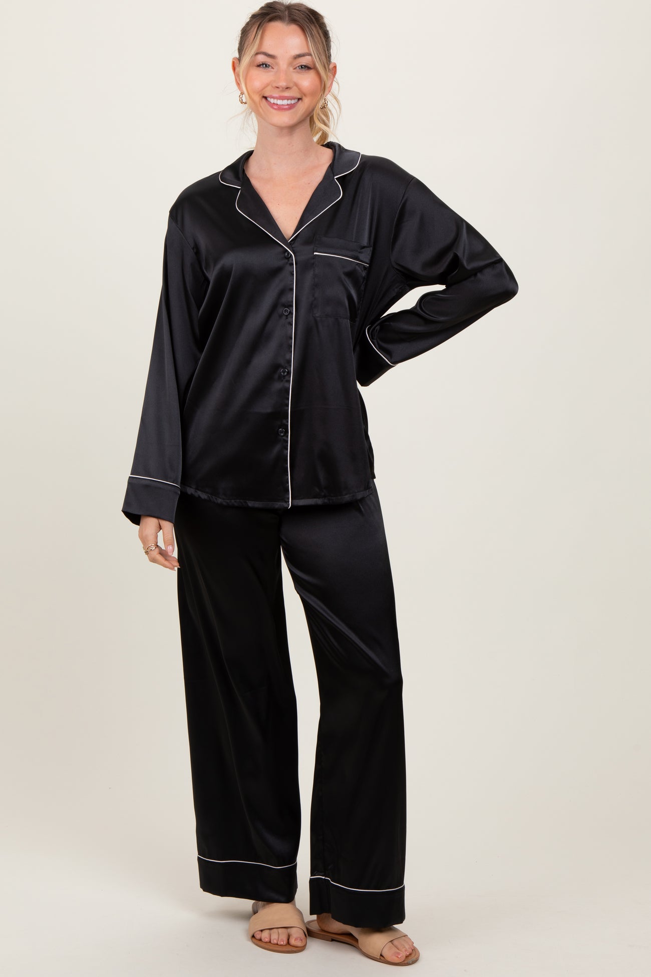 woman wearing a black satin pajama set with white piping, featuring a button-up top and wide-leg pants