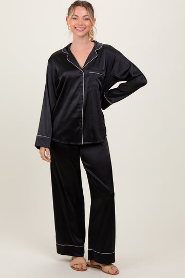 woman wearing a black satin pajama set with white piping, featuring a button-up top and wide-leg pants