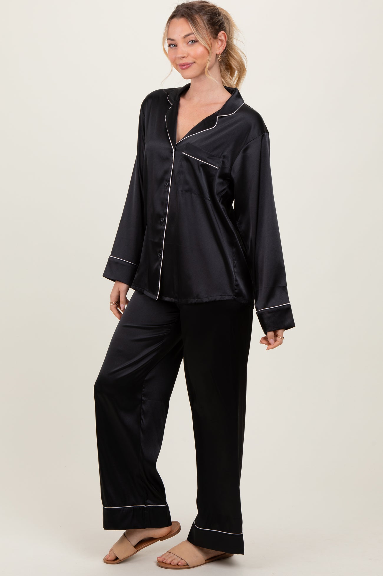 woman wearing a black satin long sleeve pajama set with white piping details