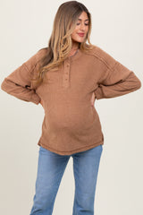 woman wearing a brown long sleeve maternity top with button details and a visible baby bump