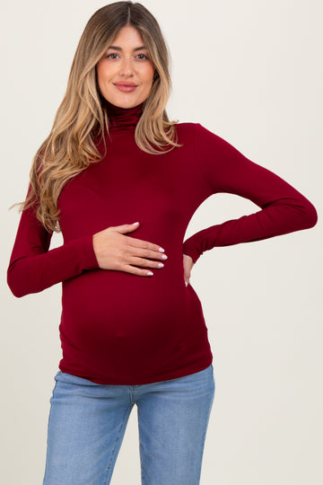 woman wearing a burgundy long sleeve maternity top and holding her baby bump