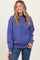 woman wearing a purple oversized sweatshirt, smiling, with long wavy hair and jeans
