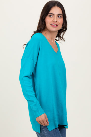 woman wearing a bright turquoise long sleeve v-neck sweater with side slits and a slightly relaxed fit