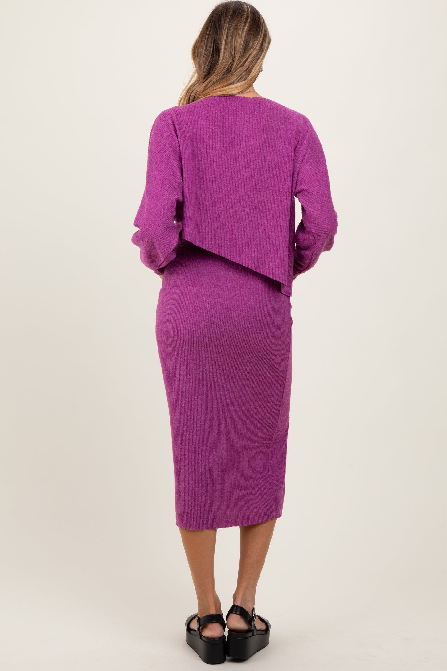 woman wearing a bright pink long-sleeve two-piece knit dress with a cropped back and fitted midi skirt