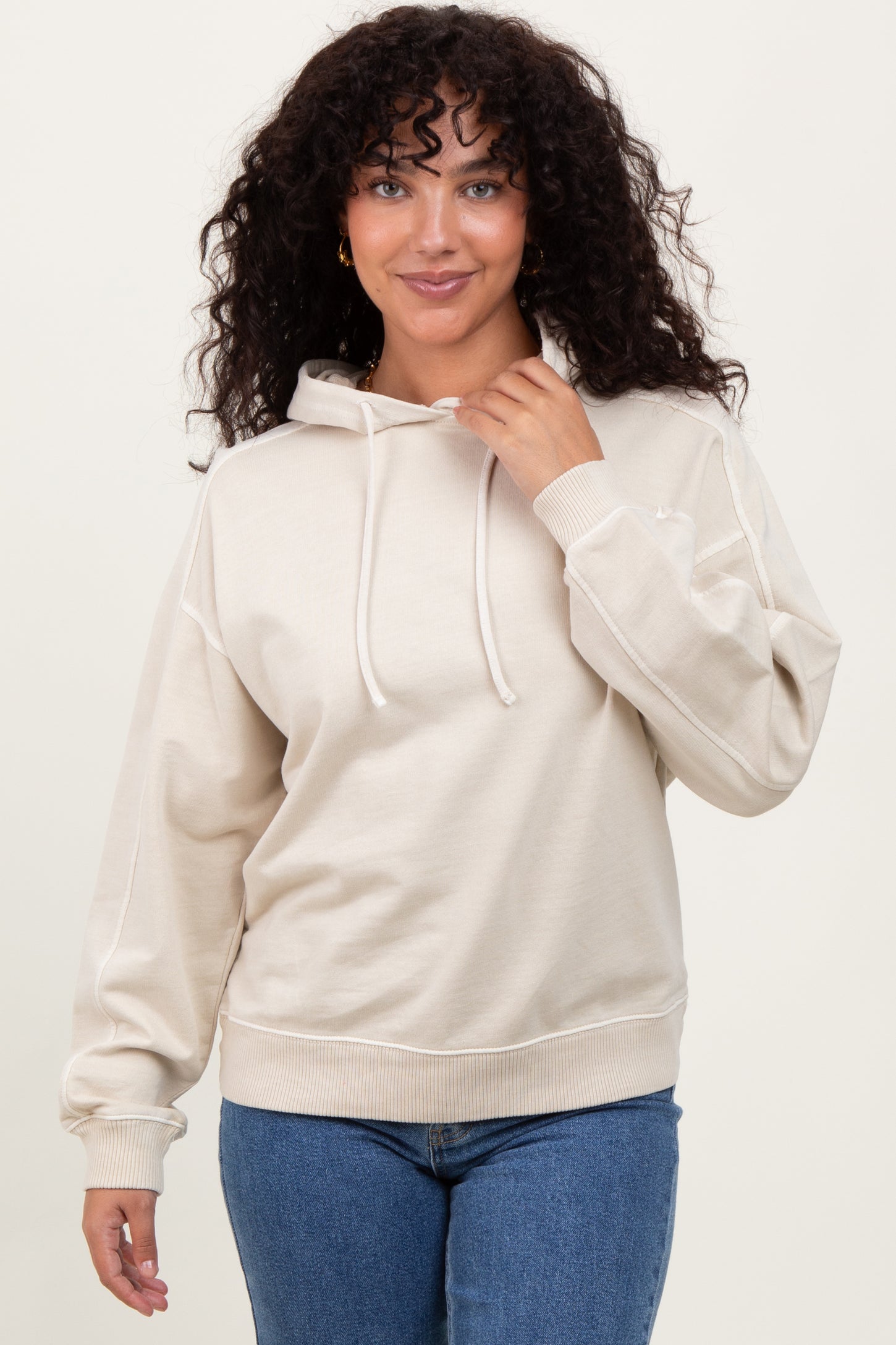woman wearing a beige hooded sweatshirt with a relaxed fit and drawstring, paired with blue jeans