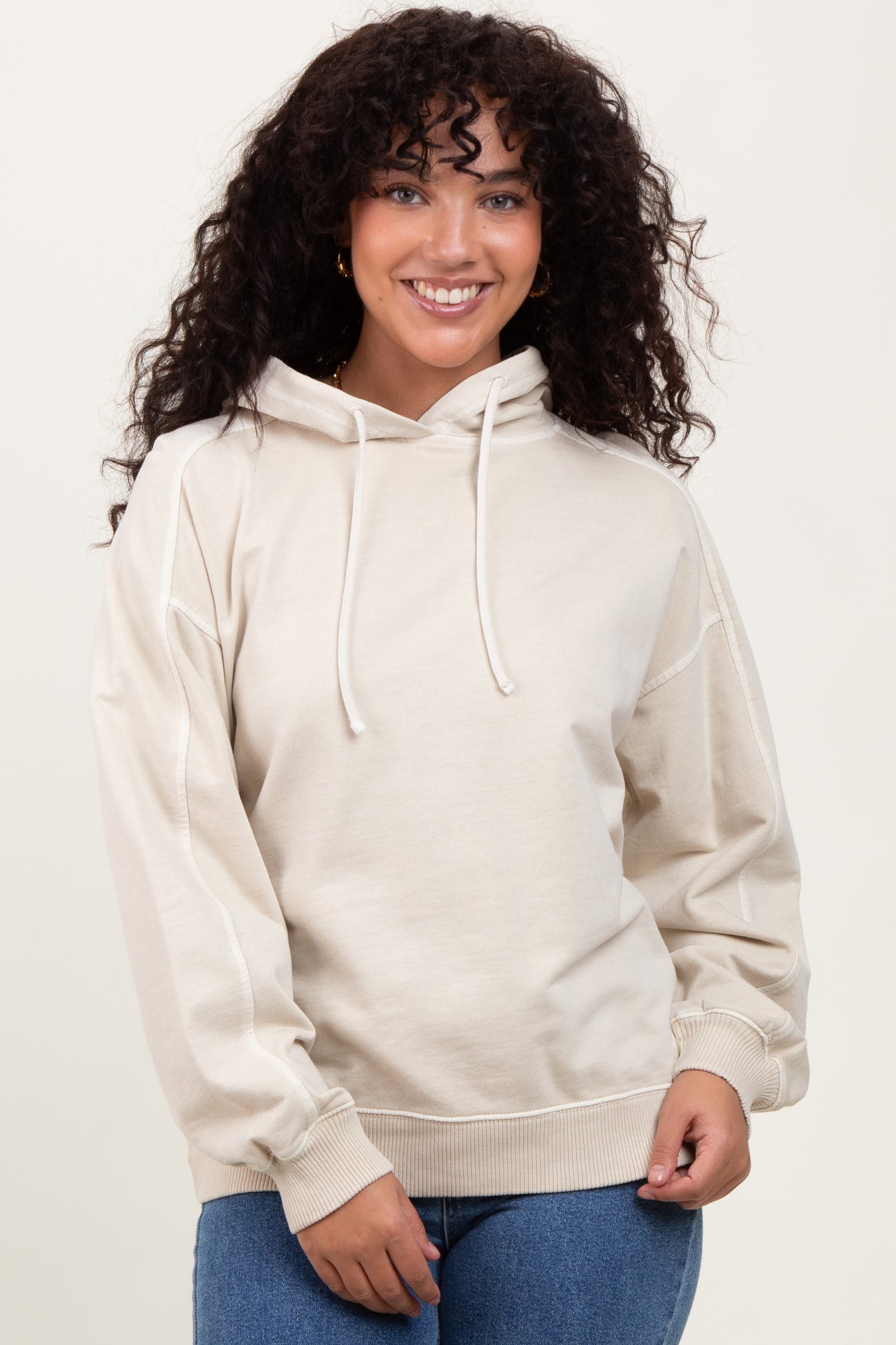 woman wearing a beige oversized hoodie with drawstrings and front pocket, styled with blue jeans