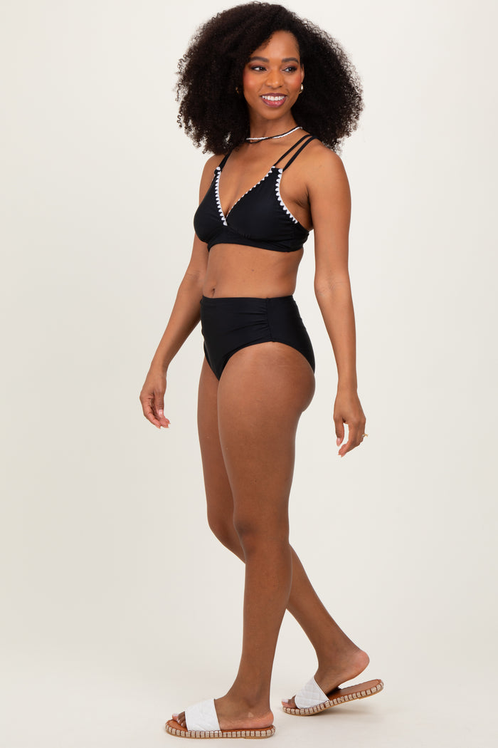 woman wearing a black bikini with beaded detail and high-waisted bottoms, standing on a neutral background