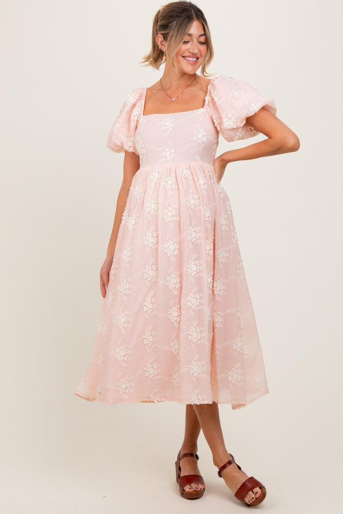 woman wearing a light pink floral maternity dress with puff sleeves and a flowing skirt, showcasing a baby bump