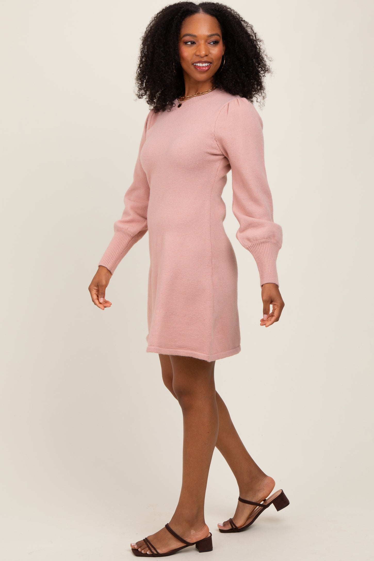 woman wearing a light pink long sleeve sweater dress with puffed sleeves and walking in a relaxed pose