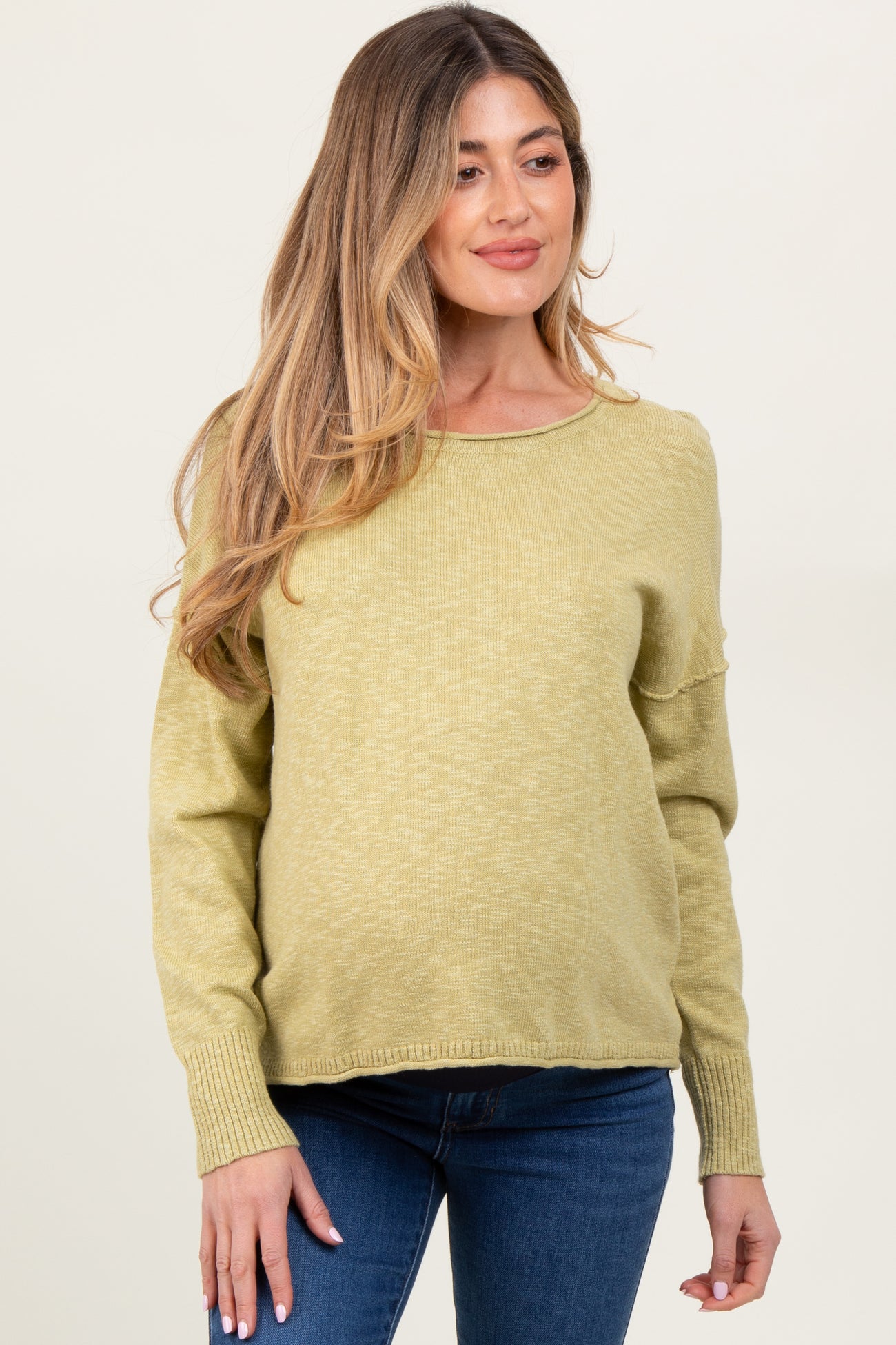 woman wearing a light olive green maternity sweater with long sleeves and relaxed fit, showing baby bump