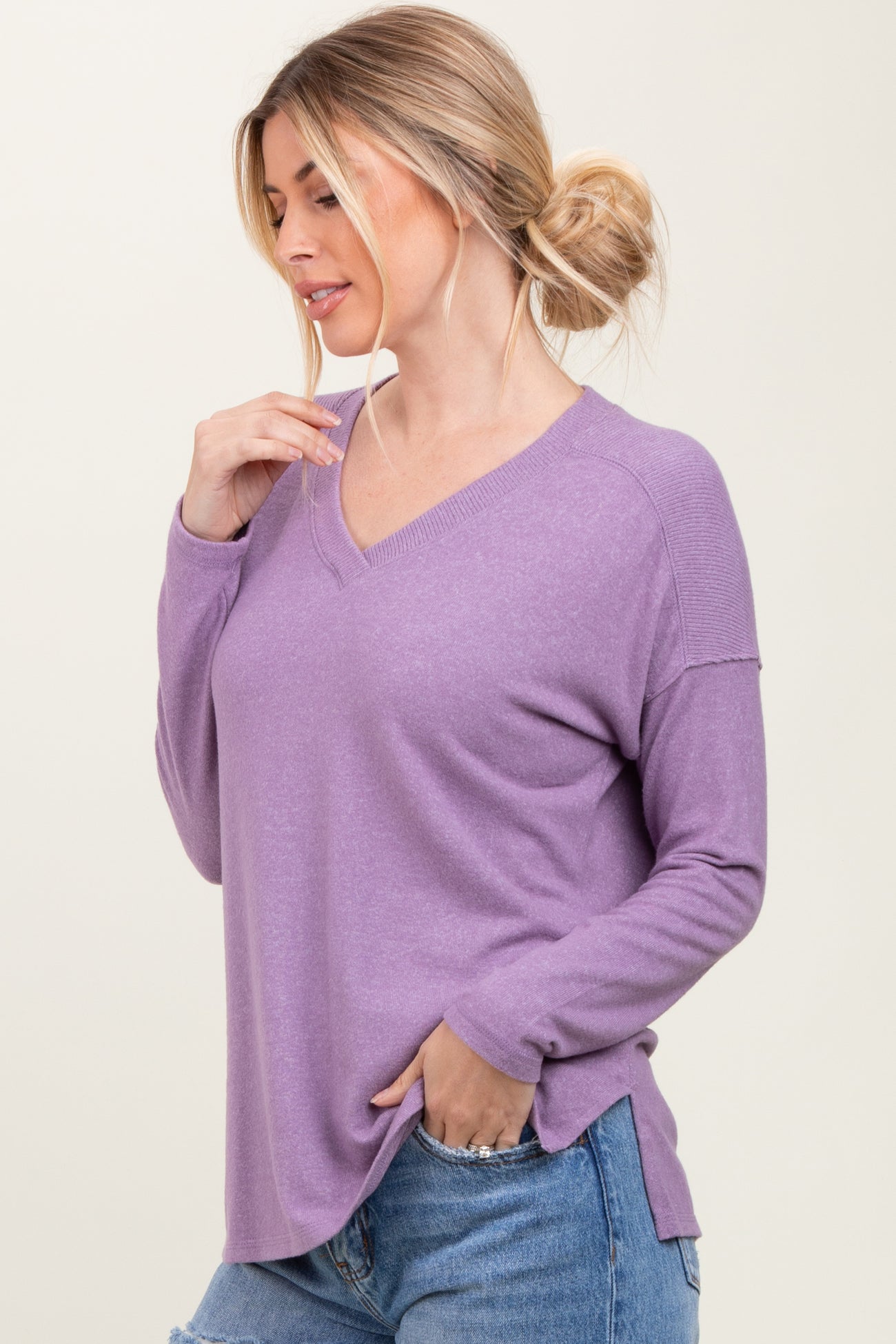 woman wearing a loose-fitting lavender long sleeve v-neck top with side slits, styled with light blue jeans