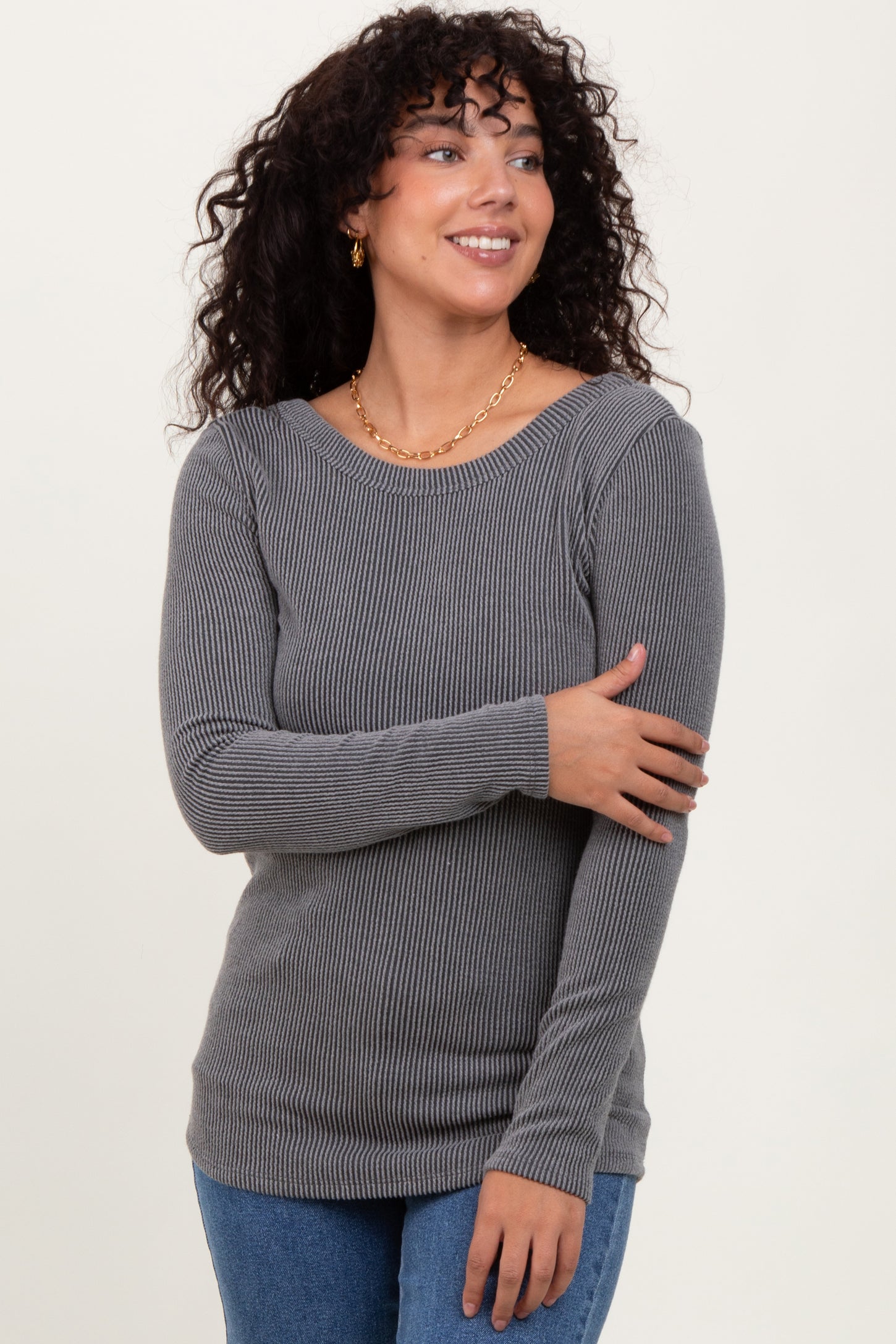 woman wearing a gray ribbed long sleeve top and smiling, with loose curls and gold earrings