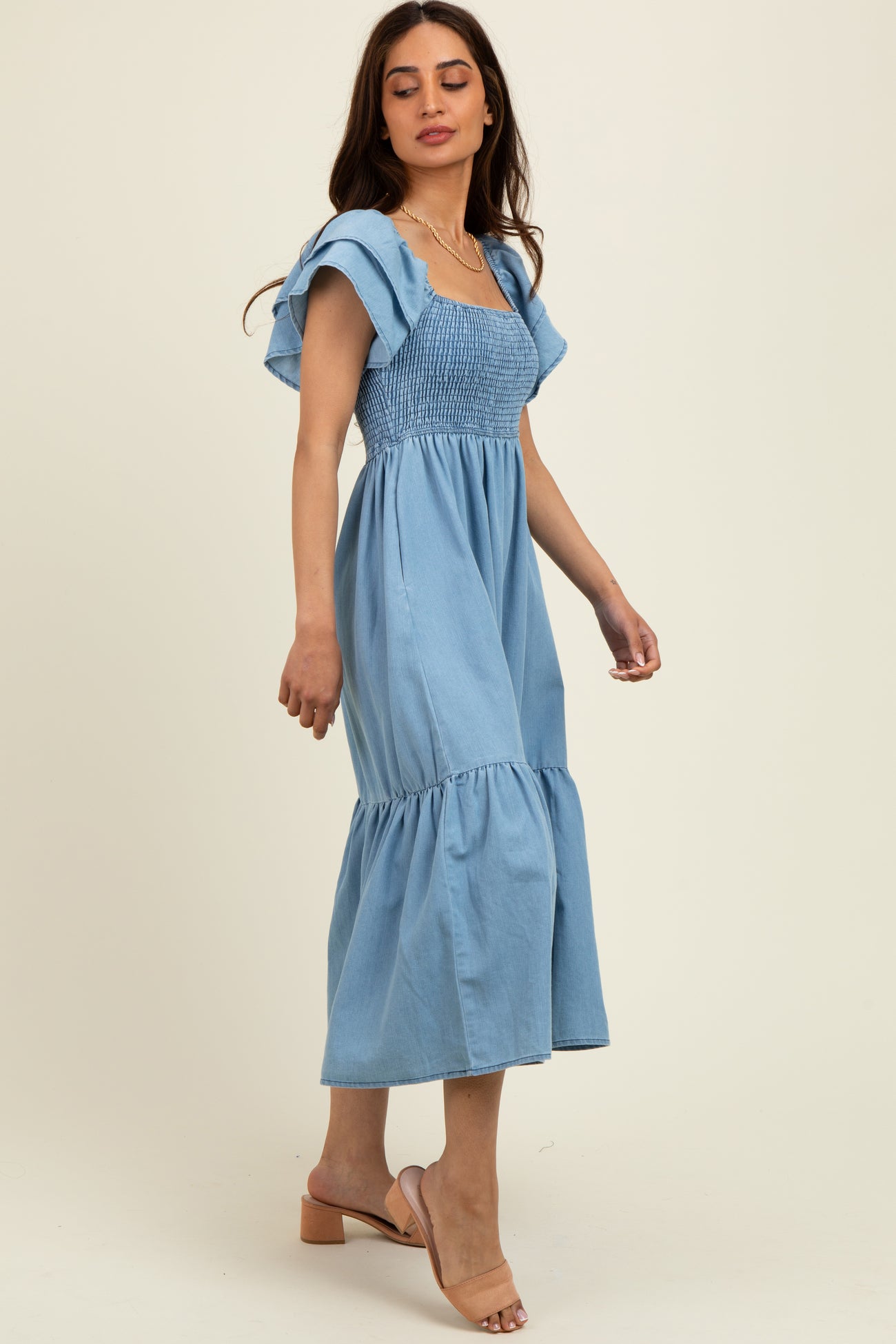 woman wearing a light blue smocked midi dress with ruffled sleeves and a tiered skirt