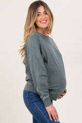 woman wearing a green long sleeve maternity sweatshirt and holding her baby bump