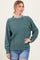 woman wearing a green ribbed long sleeve sweater with a relaxed fit and oversized cuffs, paired with distressed denim shorts
