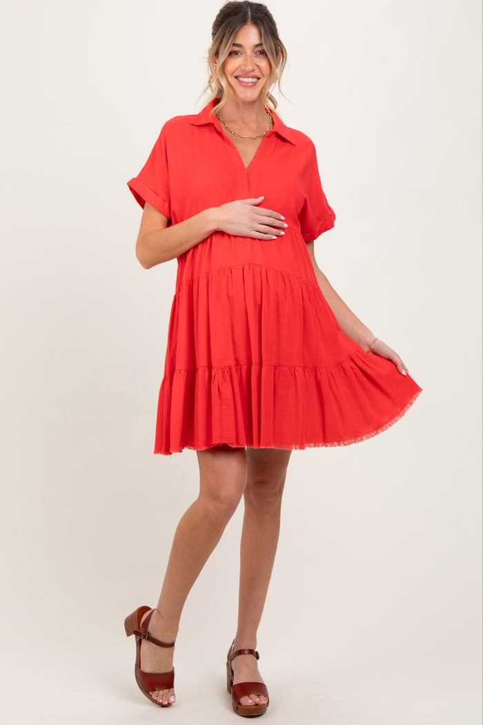 woman wearing a bright red short sleeve maternity dress with tiered detailing and holding her baby bump