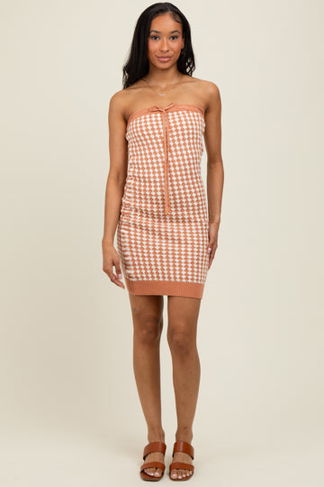 woman wearing a strapless orange and white houndstooth mini dress with a tie detail at the front and a fitted silhouette