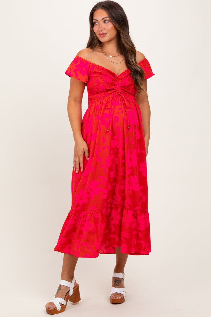 woman wearing a hot pink floral off-shoulder maternity dress with a smocked bodice and ruffle hem, showing her baby bump