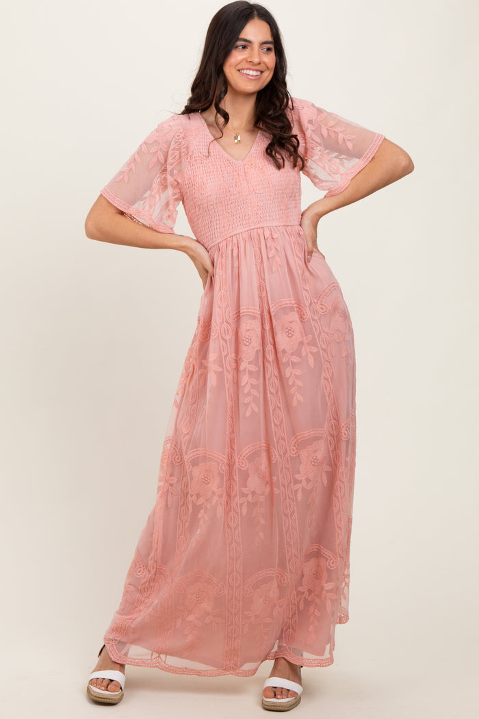 woman wearing a blush pink maxi dress with floral embroidery and short sheer sleeves, posed with hands on hips
