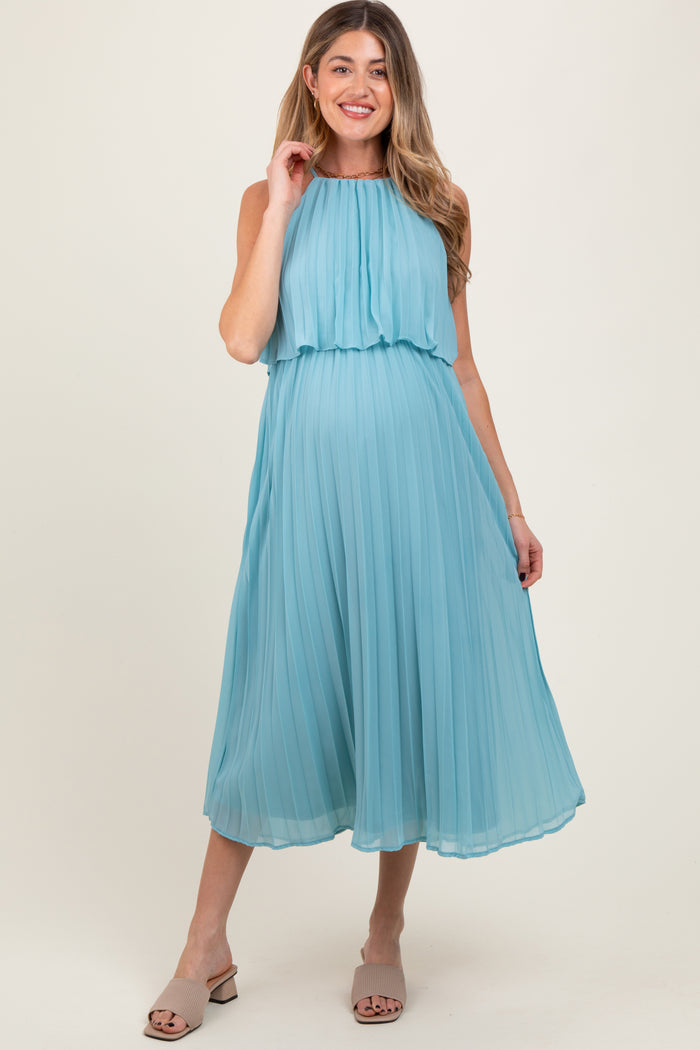 woman wearing a light blue pleated maternity dress with a high neckline and flowing skirt, showing her baby bump