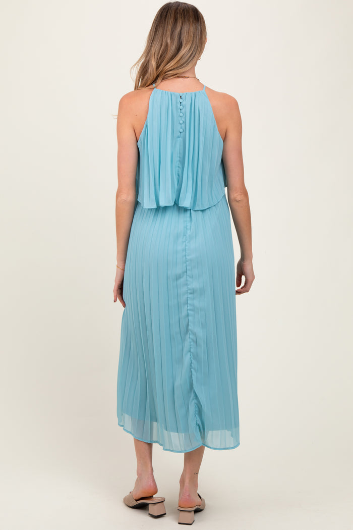 woman wearing a light blue pleated maternity dress with a flowing top and button detail at the back, showing her baby bump