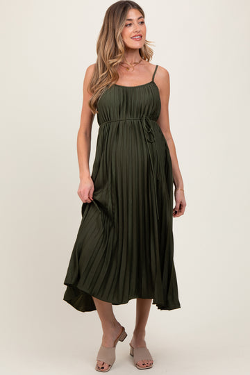 woman wearing an olive green pleated maternity dress with a tie waist and adjustable spaghetti straps