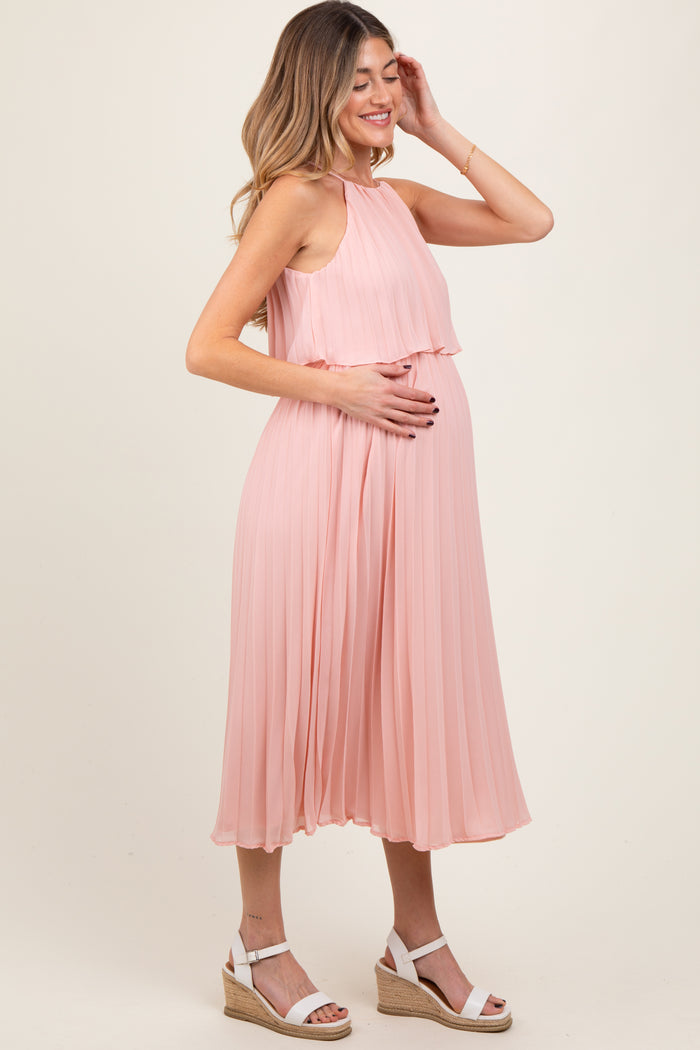 woman wearing a light pink pleated maternity dress and holding her baby bump