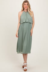 woman wearing a sage green pleated halter neck midi dress with a layered top and white heeled sandals