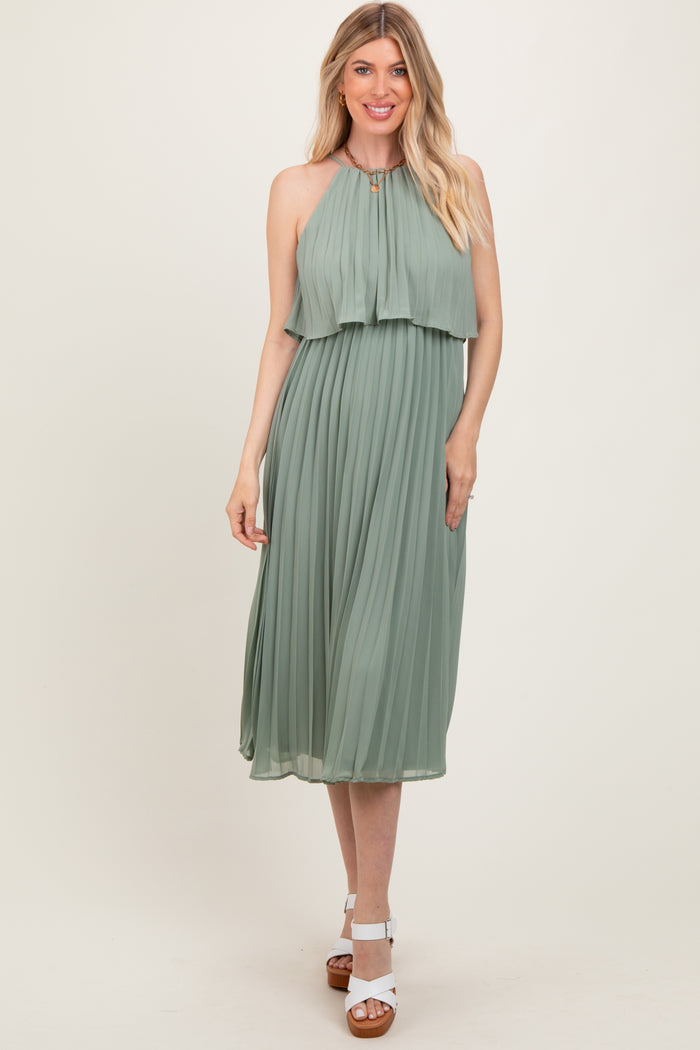 woman wearing a sage green pleated halter neck midi dress with a layered top and white heeled sandals