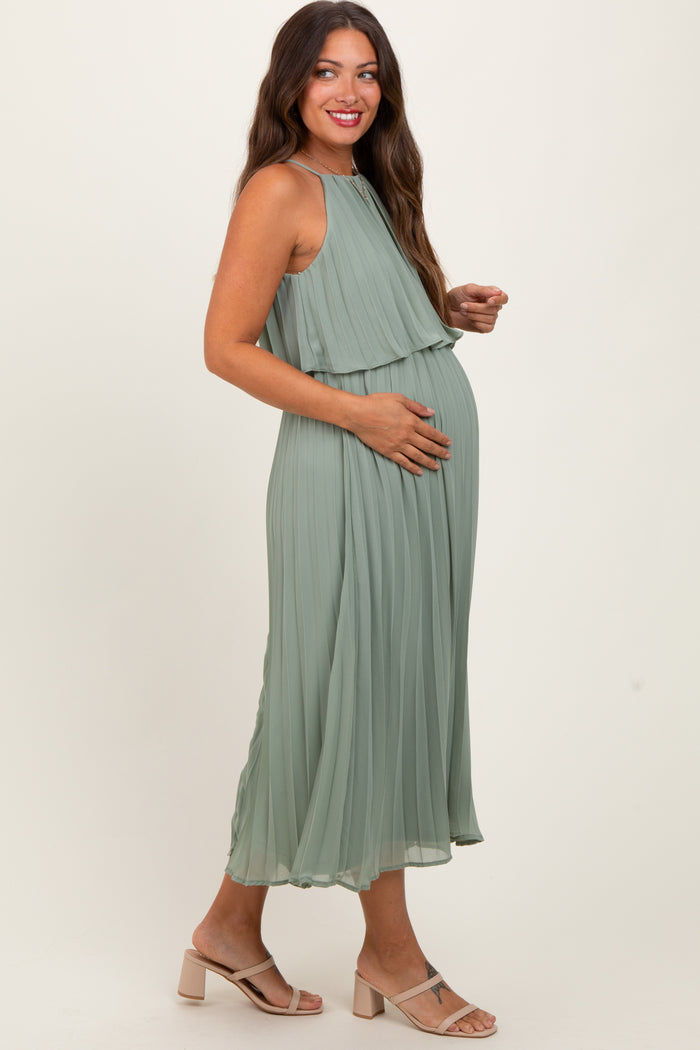 woman wearing a light green pleated maternity dress and holding her baby bump