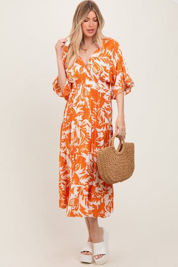 woman wearing an orange and white floral midi dress with puff sleeves, holding a straw bag and wearing platform sandals