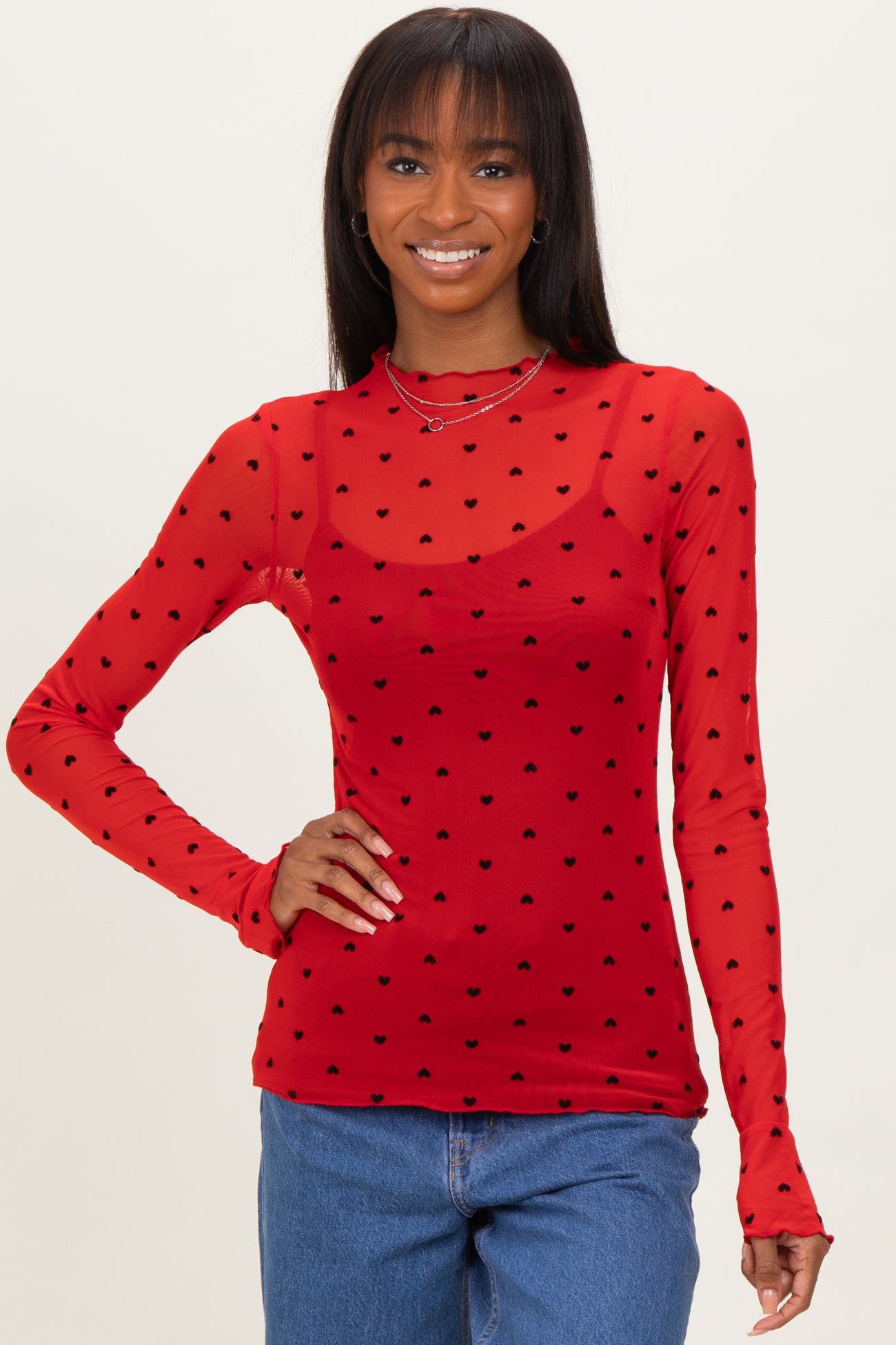 woman wearing a red long sleeve top with black heart print and sheer fabric details