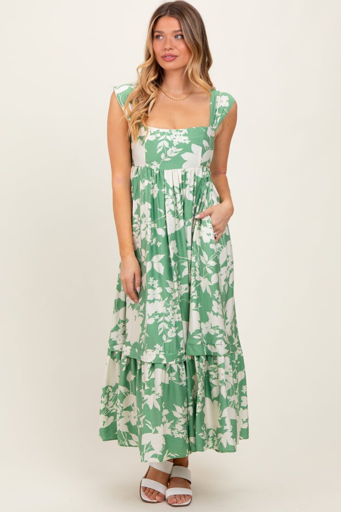 woman wearing a green floral print maxi dress with a square neckline and tiered skirt, posing with hands in pockets
