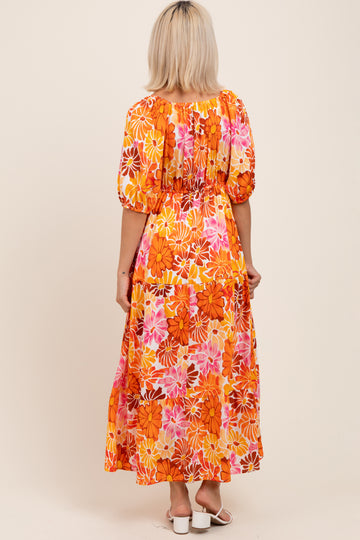 woman wearing a vibrant orange floral maternity maxi dress with puffed sleeves and a fitted bodice, seen from the back